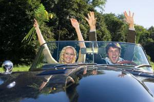 a couple raising hands inside a Jaguar E-Type convertible